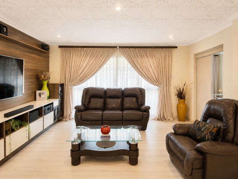 A well-maintained living room featuring a custom built-in media unit, decorative ceiling detailing, and recessed lighting, providing a comfortable and functional space.