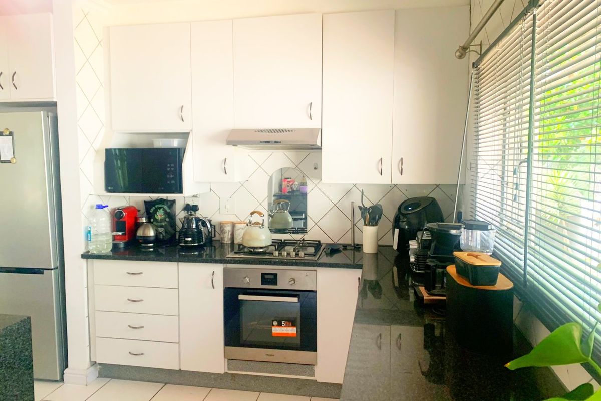 A functional kitchen featuring white cabinetry, granite countertops, a built-in oven, gas hob, and extractor fan with tiled backsplash and flooring.