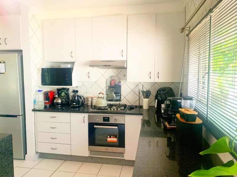 A functional kitchen featuring white cabinetry, granite countertops, a built-in oven, gas hob, and extractor fan with tiled backsplash and flooring.