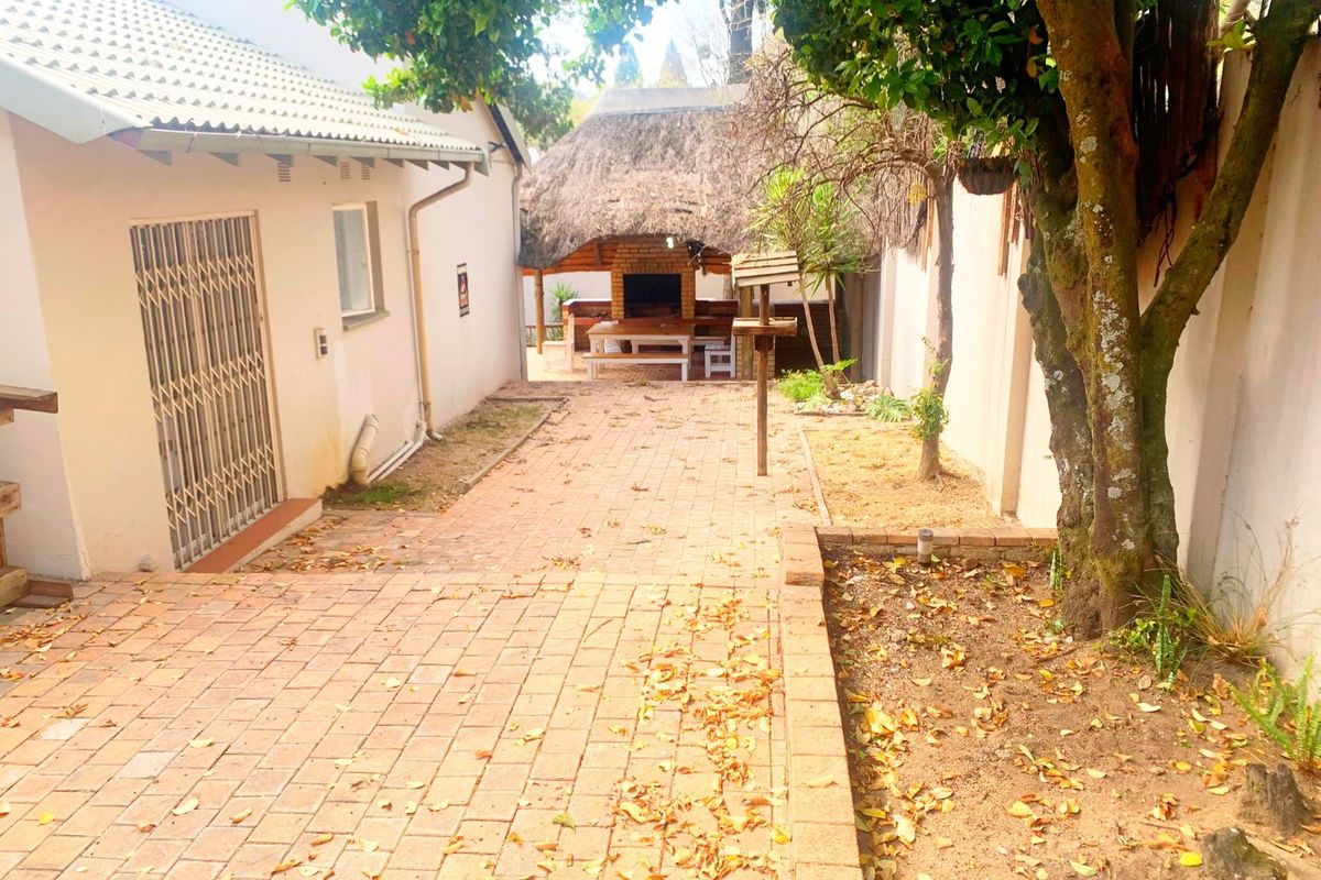 Rear courtyard featuring brick paving, a thatched lapa with a built-in braai, and established garden beds.