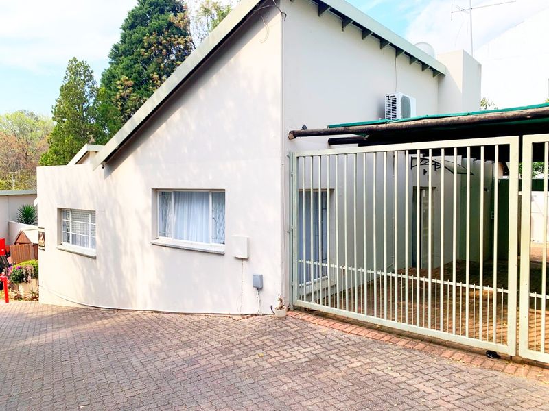 Front exterior view of the townhouse featuring a paved driveway, secure metal gate, and exterior wall-mounted air conditioning unit.