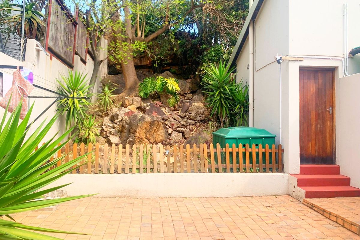 A private rear courtyard featuring a paved patio, a tiered rockery garden, and direct access to the property via a timber door.