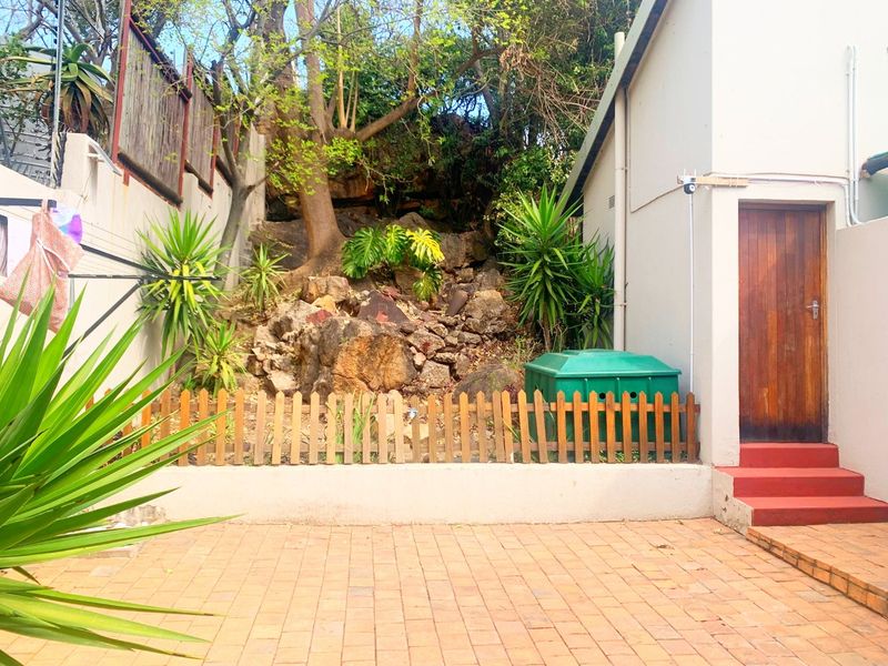 A private rear courtyard featuring a paved patio, a tiered rockery garden, and direct access to the property via a timber door.