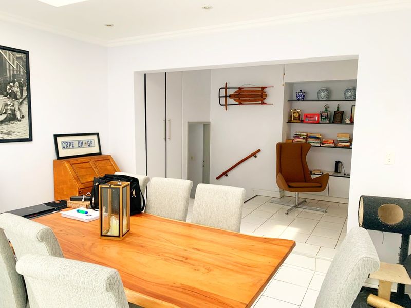 An open-plan living and dining area featuring tiled flooring, built-in shelving, and integrated storage cupboards, providing a versatile and functional layout.