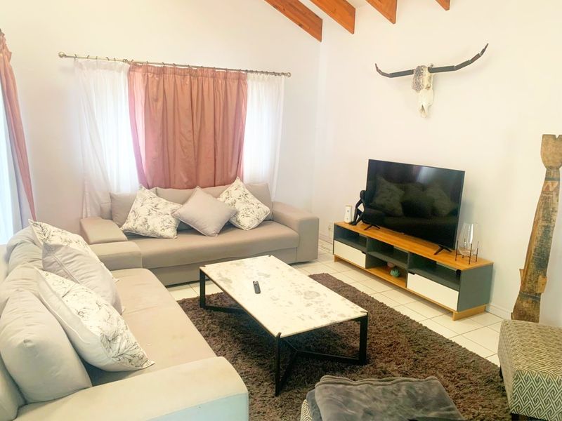 A comfortable living room featuring exposed timber ceiling beams and tiled flooring, offering a bright and inviting space for relaxation.