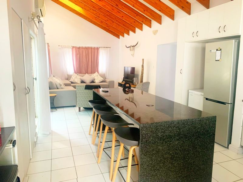 Open-plan living and kitchen area featuring a large granite island, exposed timber ceiling beams, and tiled flooring throughout.