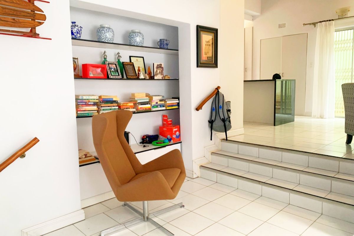 A split-level living area featuring white tiled flooring, built-in wall shelving, and a staircase with a wooden handrail leading to an elevated space.
