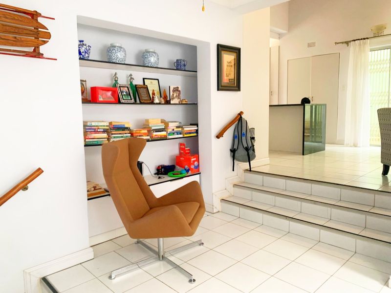 A split-level living area featuring white tiled flooring, built-in wall shelving, and a staircase with a wooden handrail leading to an elevated space.