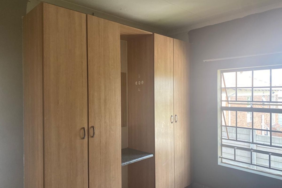 A bedroom featuring built-in wooden cupboards with a central vanity area, tiled flooring, and security bars on the window.