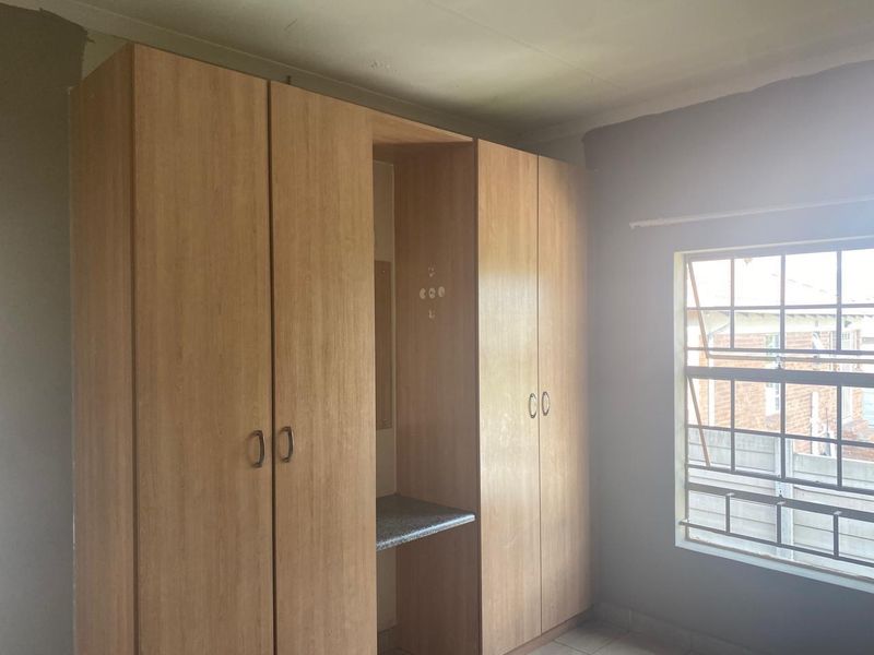 A bedroom featuring built-in wooden cupboards with a central vanity area, tiled flooring, and security bars on the window.