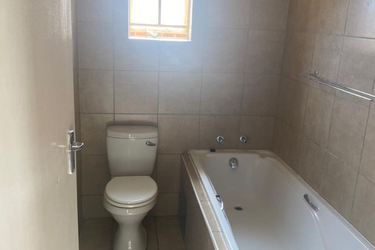 A functional bathroom featuring a built-in bathtub, toilet, and neutral wall and floor tiling.