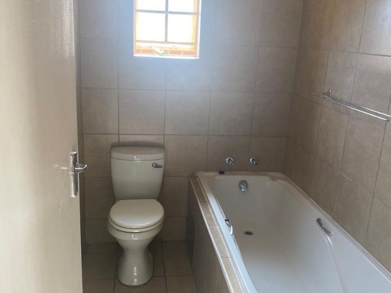 A functional bathroom featuring a built-in bathtub, toilet, and neutral wall and floor tiling.