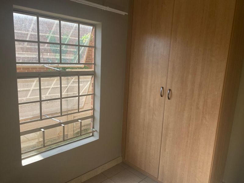 A bedroom featuring built-in wooden wardrobes, tiled flooring, and a window fitted with security bars.