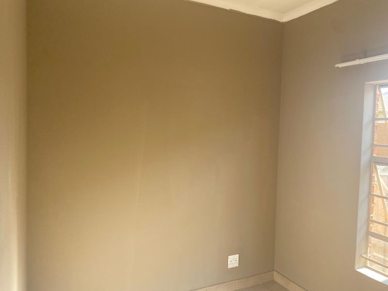 An empty bedroom featuring neutral painted walls, tiled flooring, and a window fitted with security bars.