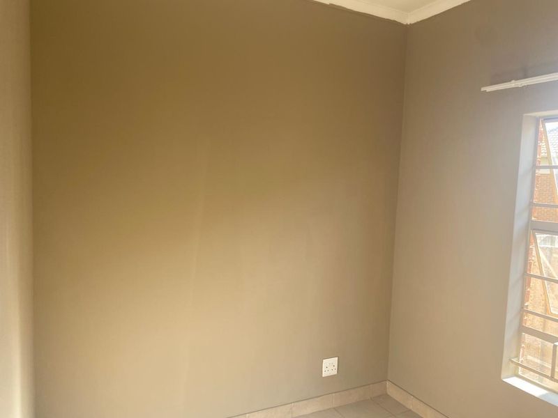 An empty bedroom featuring neutral painted walls, tiled flooring, and a window fitted with security bars.