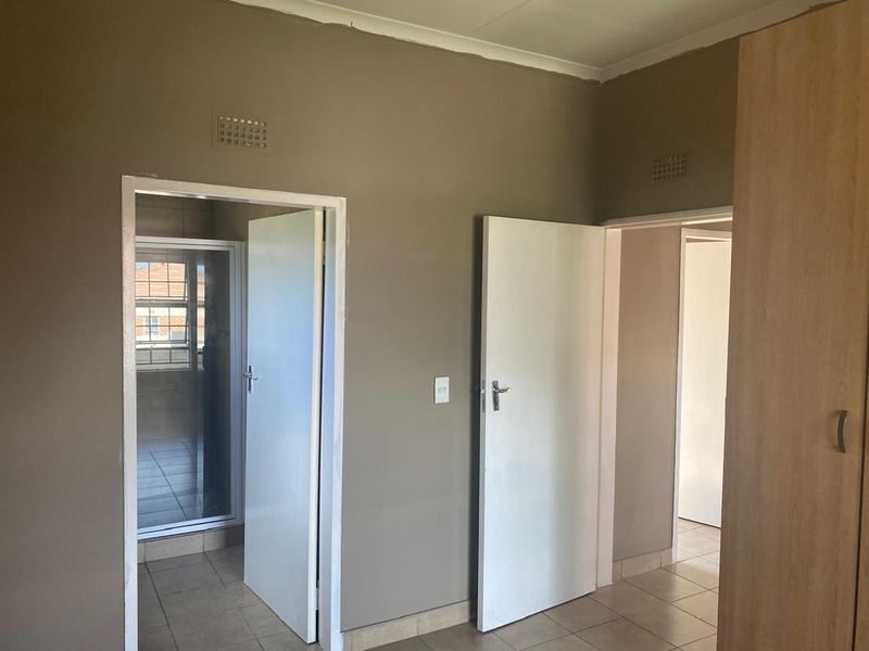 A neutral-toned bedroom featuring tiled flooring, built-in wardrobe storage, and direct access to an en-suite bathroom.
