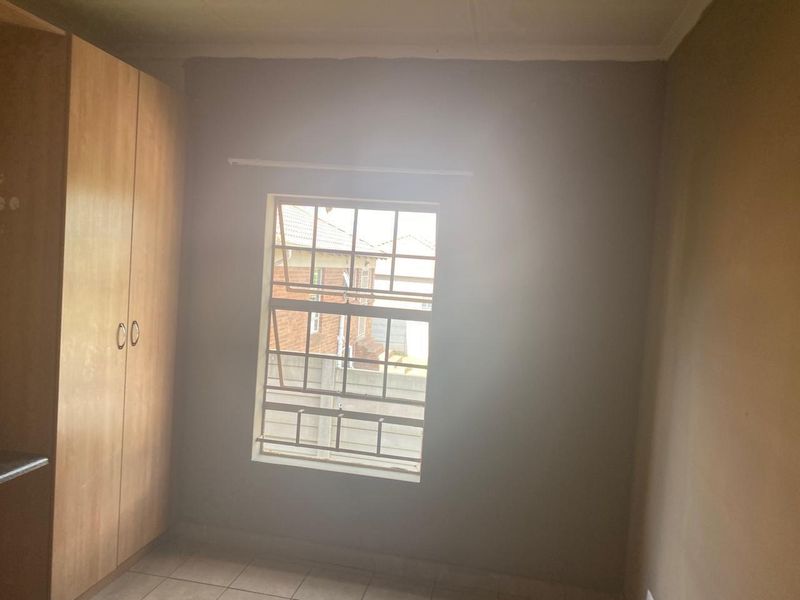 A simple bedroom featuring tiled flooring, a built-in wardrobe, and a window fitted with security bars.