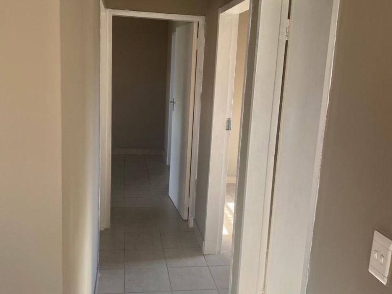 A neutral-toned hallway featuring tiled flooring and multiple internal doorways providing access to adjacent rooms.
