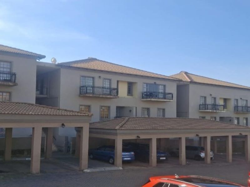 Front elevation of a multi-story townhouse complex featuring covered parking bays, tiled roofing, and balconies with wrought iron railings.