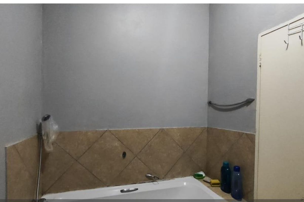 A bathroom featuring a bathtub with a handheld shower head and tiled splashback, requiring minor maintenance and cosmetic updates.