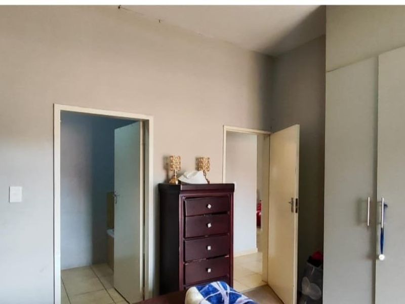 A bedroom featuring built-in cupboards and access to adjacent rooms, showing signs of wear including ceiling cracks.