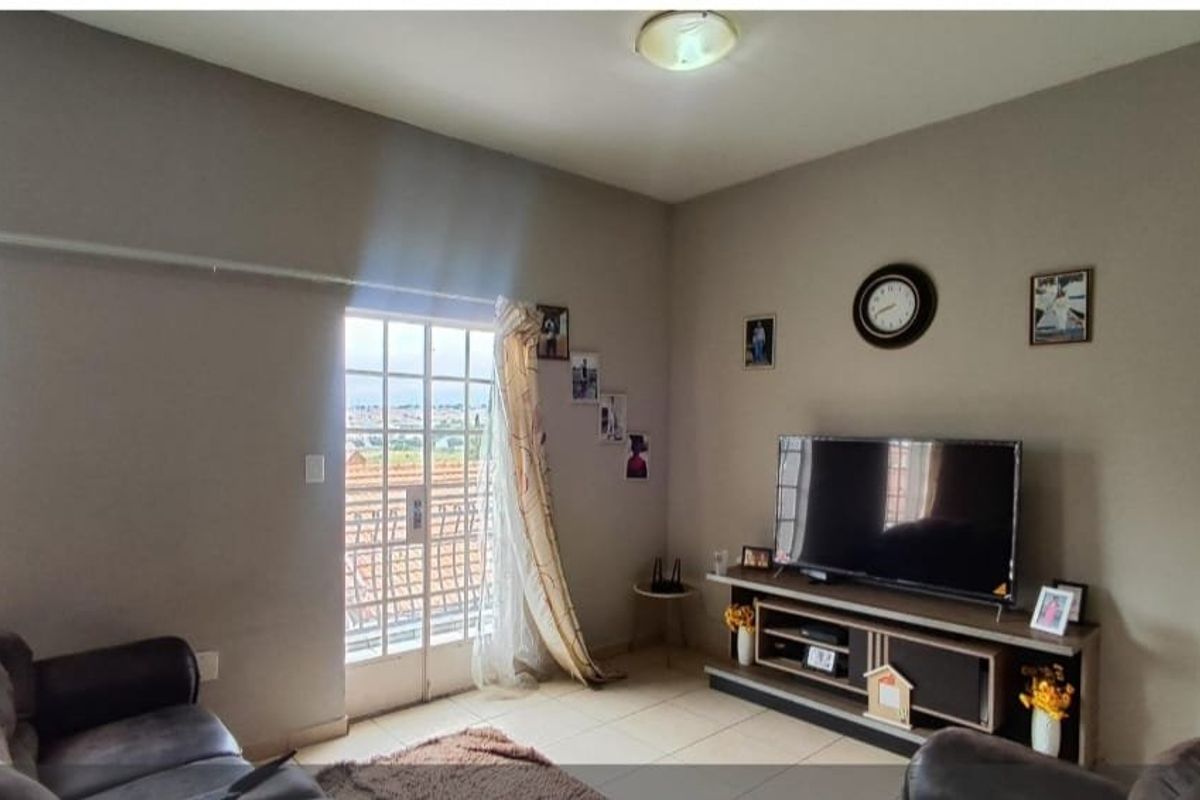 A comfortable living room featuring tiled flooring, a sliding door with a security gate, and neutral wall tones.