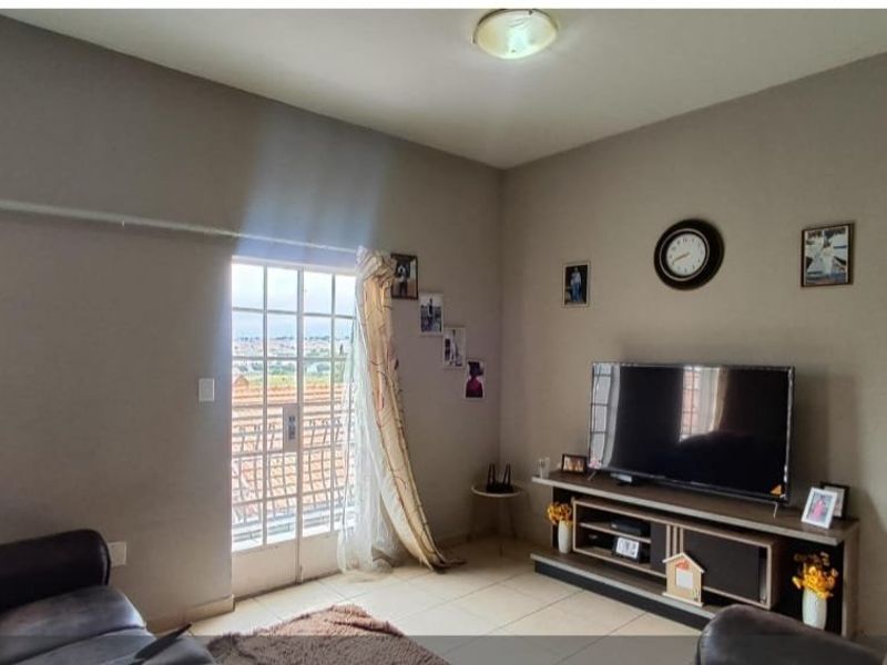 A comfortable living room featuring tiled flooring, a sliding door with a security gate, and neutral wall tones.