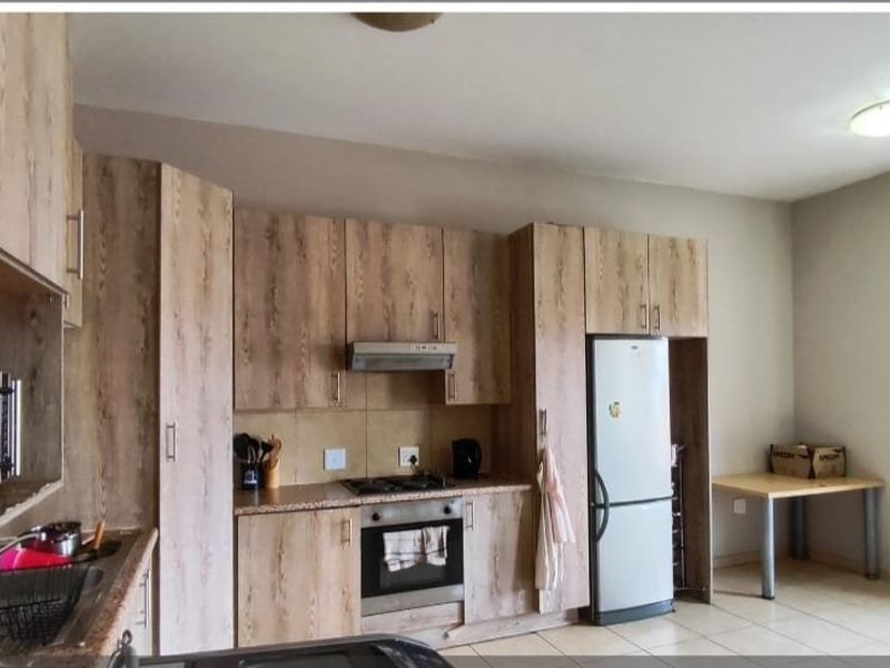 Functional kitchen featuring wood-look laminate cabinetry, built-in oven, gas hob, extractor fan, and tiled flooring with a practical layout.