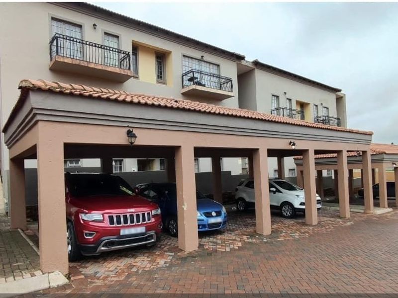 Exterior view of a townhouse complex featuring covered parking bays, paved driveway, and upper-level balconies with metal railings.