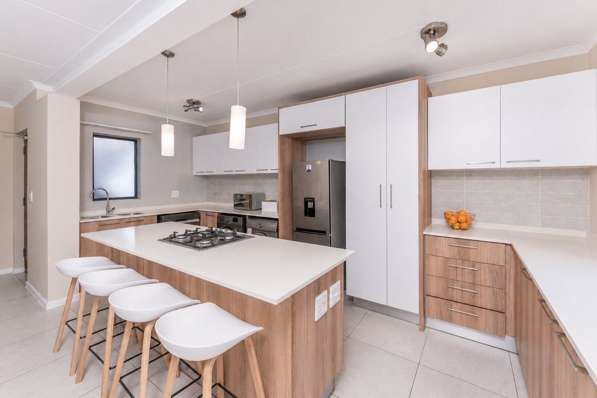 Modern kitchen featuring a central island with a gas hob, stone countertops, ample built-in cabinetry, and tiled flooring in an open-plan layout.
