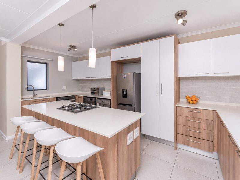 Modern kitchen featuring a central island with a gas hob, stone countertops, ample built-in cabinetry, and tiled flooring in an open-plan layout.