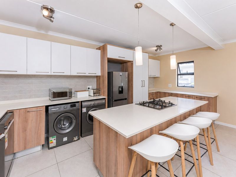 Modern kitchen featuring wood-finish cabinetry, stone countertops, a central island with a gas hob, and integrated laundry appliances.