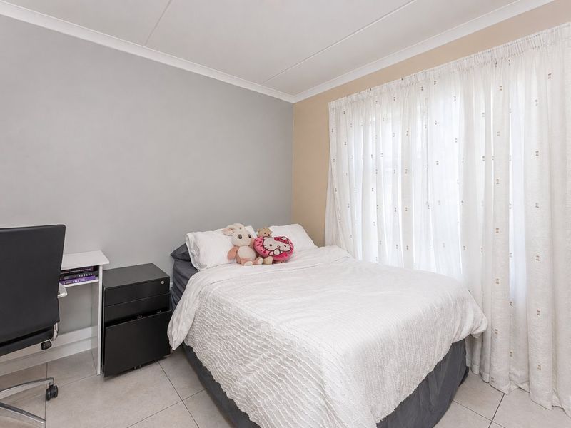 A functional bedroom featuring neutral wall tones, tiled flooring, and large windows dressed with curtains.