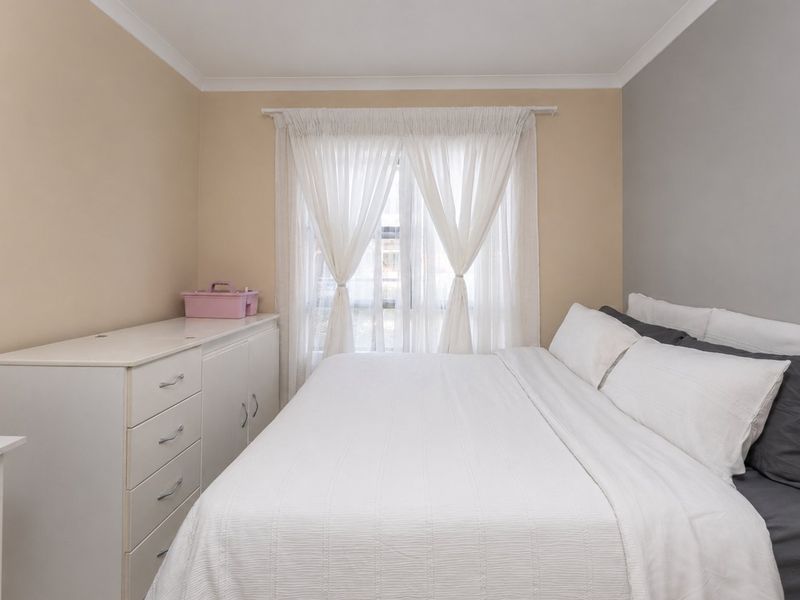 A neutrally painted bedroom featuring a window with sheer curtains and coving detail.