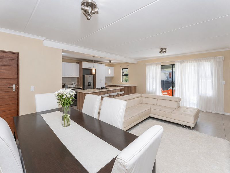 Spacious open-plan living and dining area featuring a modern kitchen with a central island, tiled floors, and direct access to the patio.