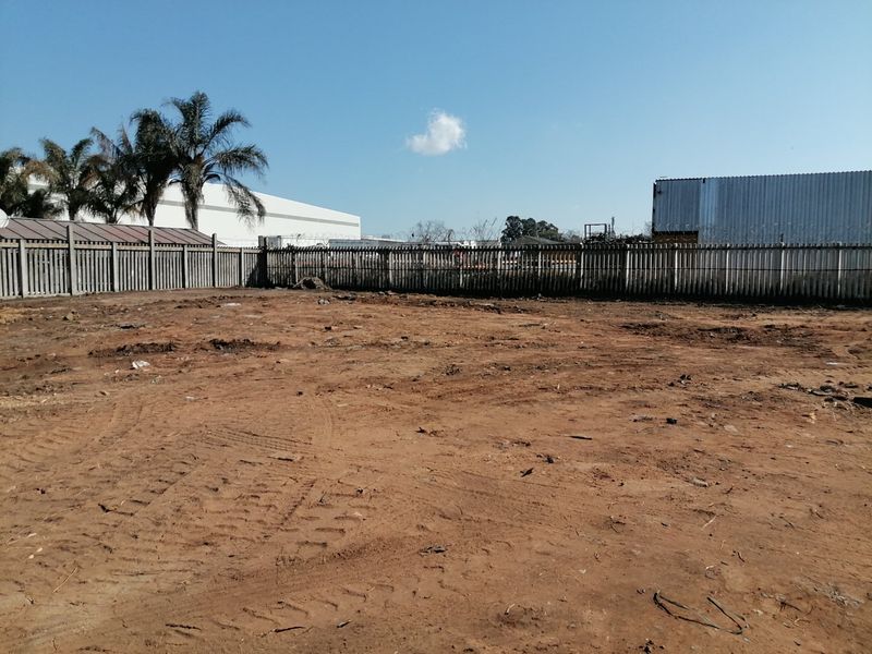 A vacant residential plot featuring cleared earth and secure concrete palisade perimeter fencing with razor wire.