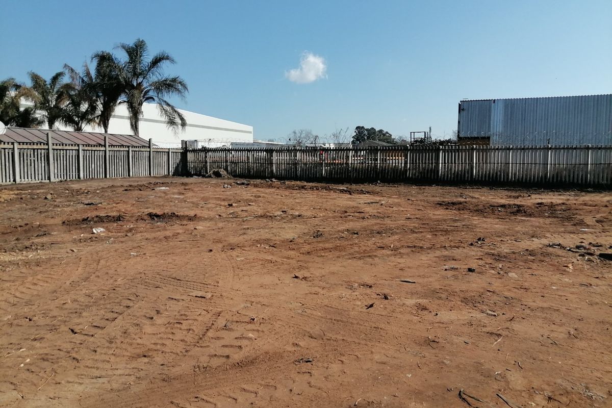 A vacant residential plot featuring cleared earth and secure concrete palisade perimeter fencing with razor wire.