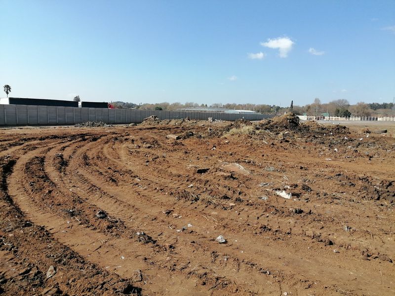 A vacant residential plot featuring cleared earth, tire tracks, and a precast concrete boundary wall along the perimeter.