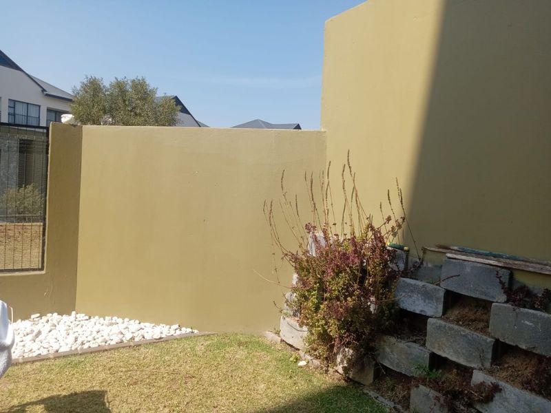 A private rear garden area featuring a painted boundary wall, a small lawn, and an unfinished concrete block retaining wall.