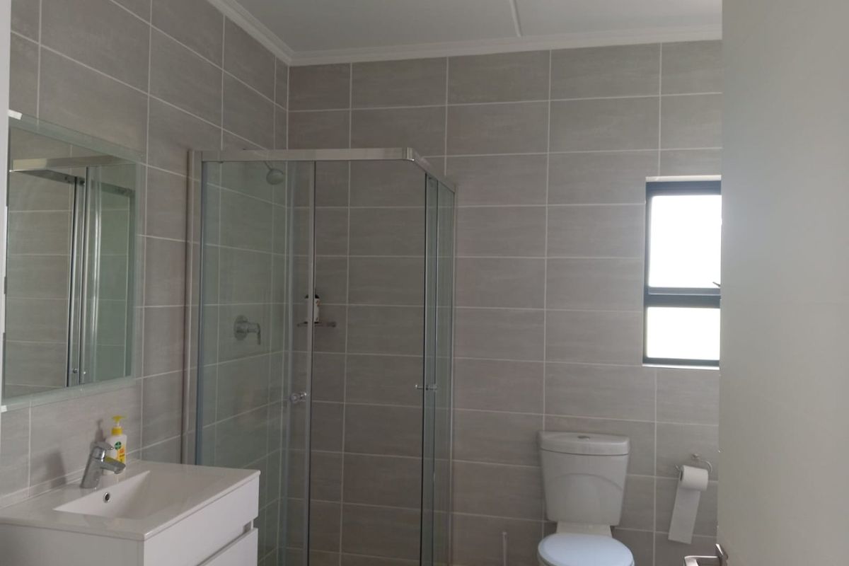 A modern bathroom featuring a glass shower enclosure, a white vanity with basin, and neutral grey wall tiles.