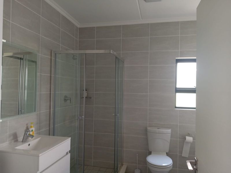 A modern bathroom featuring a glass shower enclosure, a white vanity with basin, and neutral grey wall tiles.