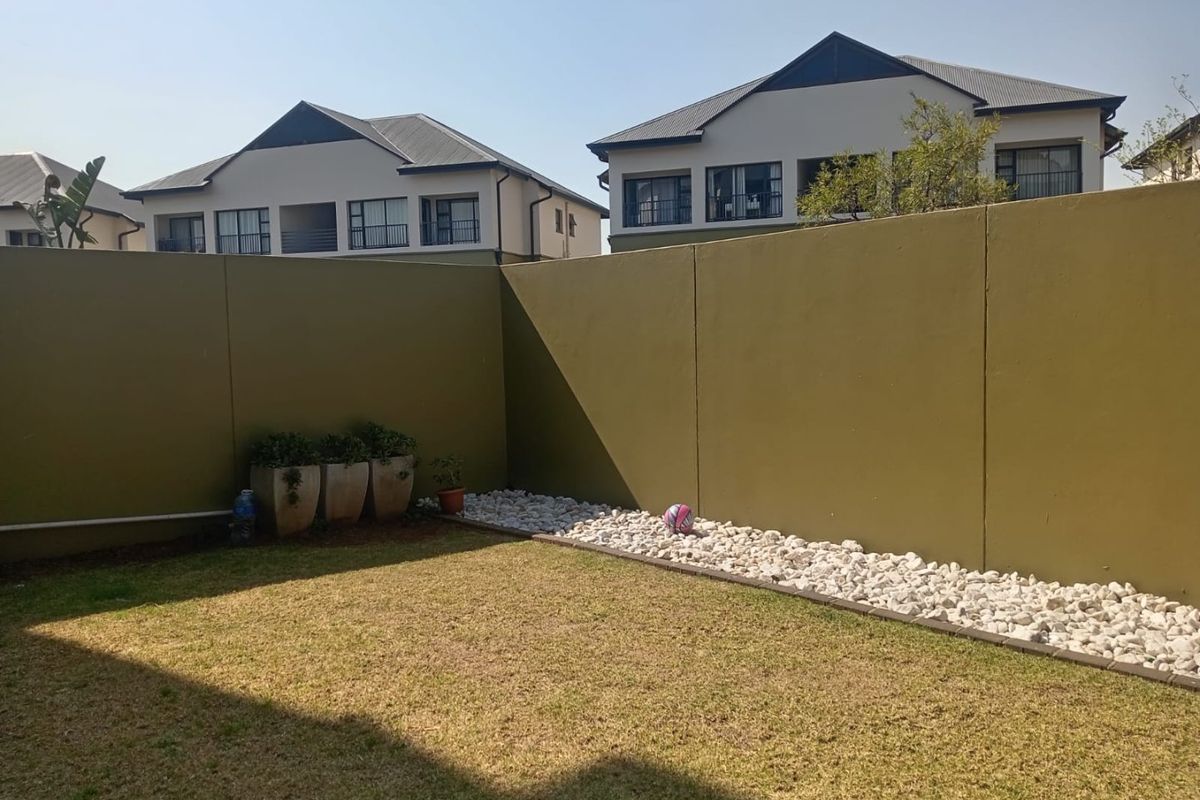 A private rear garden area featuring a well-maintained lawn, decorative pebble landscaping, and high boundary walls for added privacy.