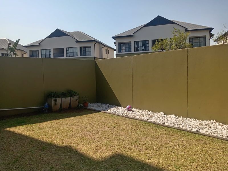A private rear garden area featuring a well-maintained lawn, decorative pebble landscaping, and high boundary walls for added privacy.