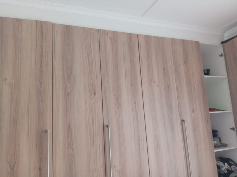 A bedroom featuring modern wood-grain finish built-in wardrobes with sleek metal handles and decorative ceiling coving.