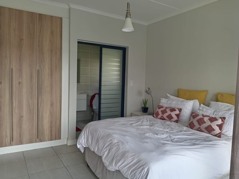 A well-maintained bedroom featuring built-in wood-finish wardrobes, tiled flooring, and an adjoining en-suite bathroom with a sliding privacy door.