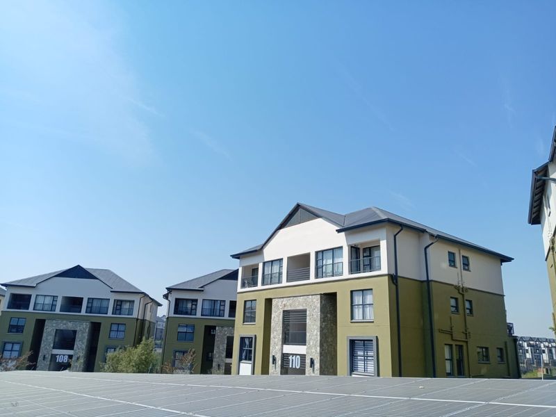 Exterior view of modern apartment blocks featuring stone cladding, balconies, and integrated solar panel arrays on the roof.