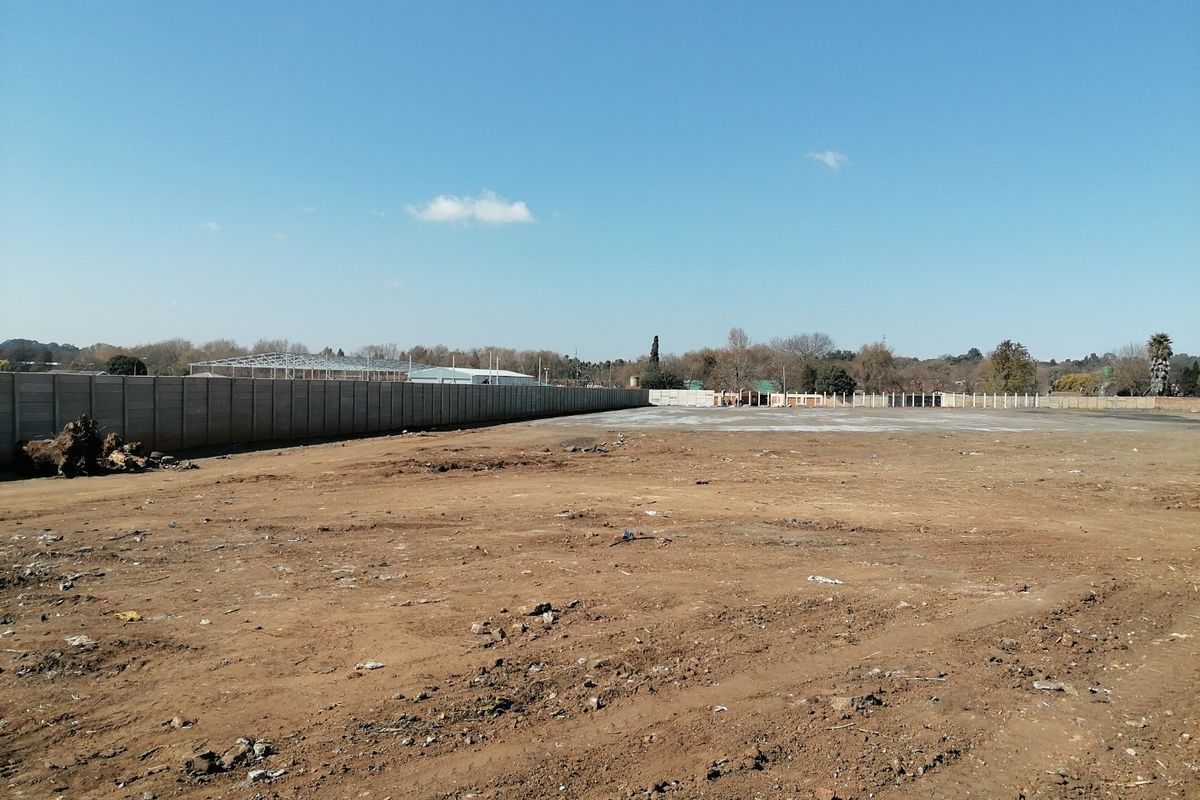A large, cleared vacant residential plot featuring a long precast concrete boundary wall, offering a blank canvas for future development.