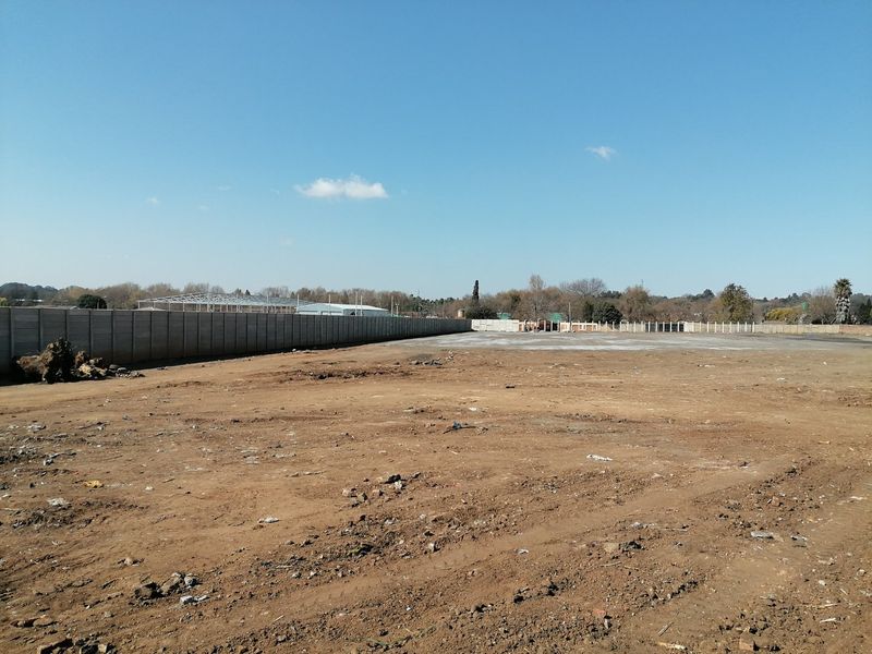 A large, cleared vacant residential plot featuring a long precast concrete boundary wall, offering a blank canvas for future development.