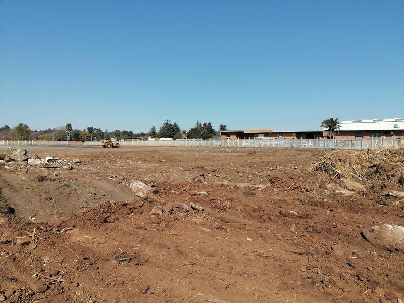 A large, cleared vacant residential plot featuring perimeter fencing and visible ground debris, ready for development.