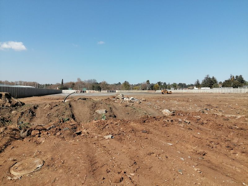 A vacant residential plot featuring cleared land, a precast concrete boundary wall, and uneven terrain, ready for development.